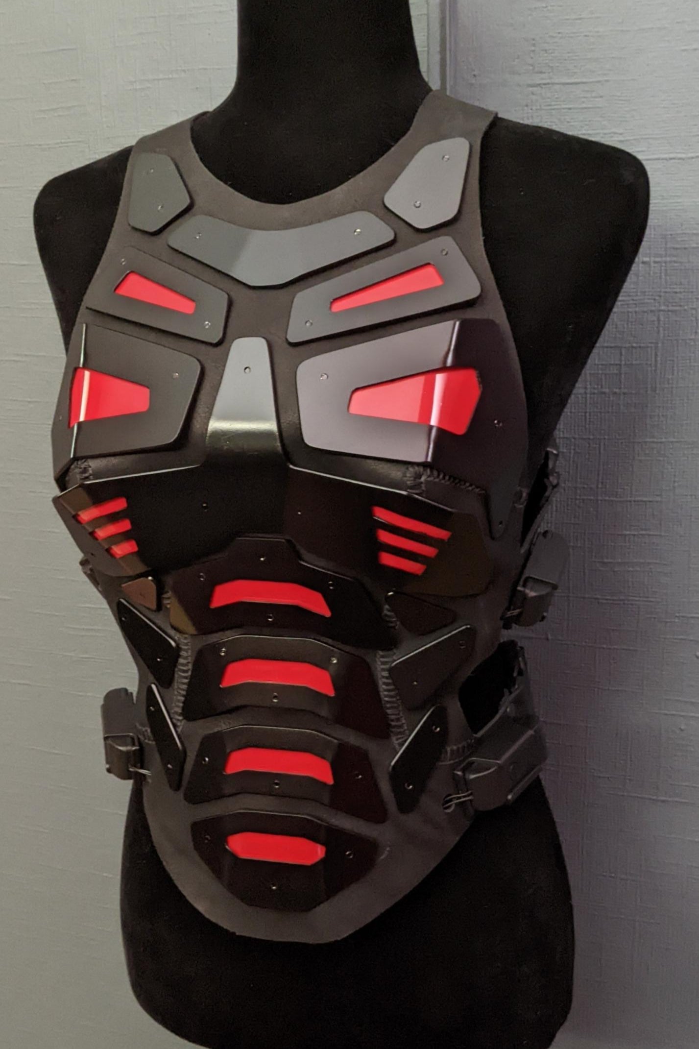Mannequin wearing futuristic torso armor in black and grey with glowing red lights