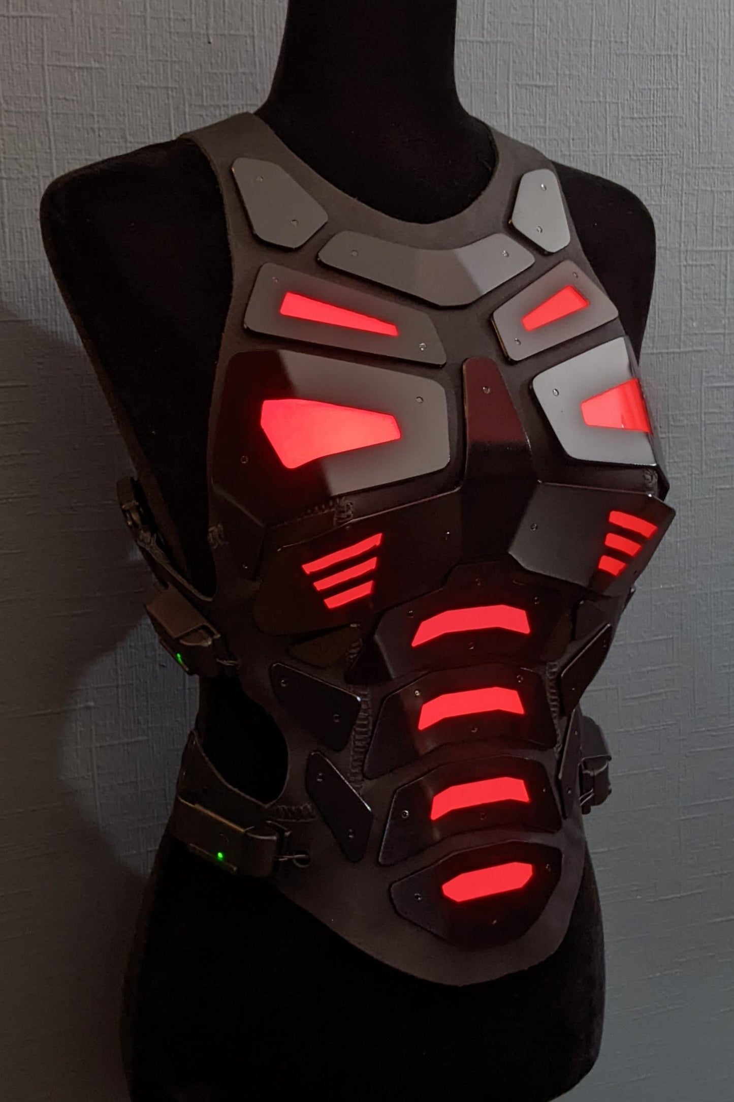 Mannequin wearing futuristic torso armor in black and grey with glowing red lights