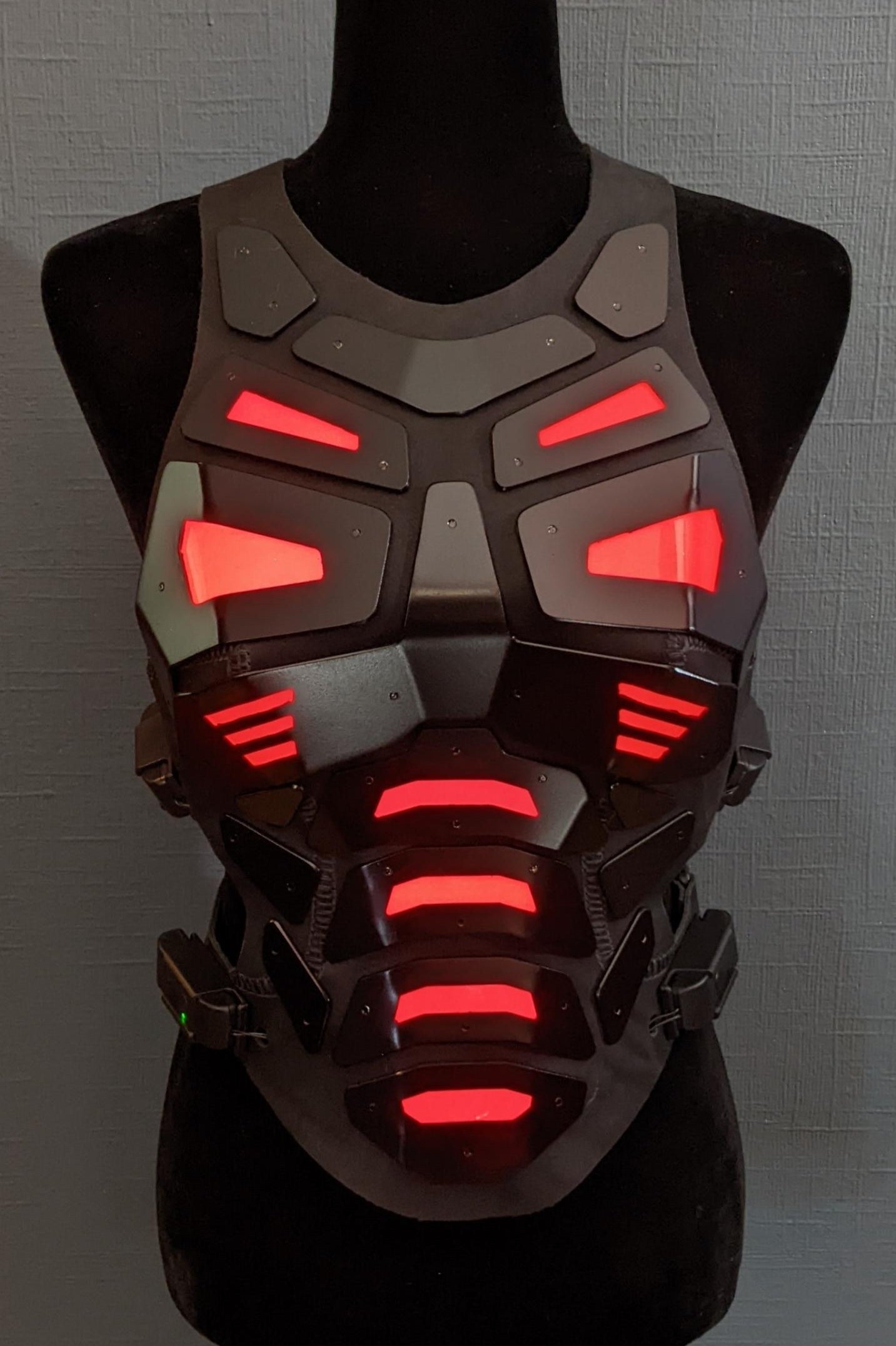 Mannequin wearing futuristic torso armor in black and grey with glowing red lights
