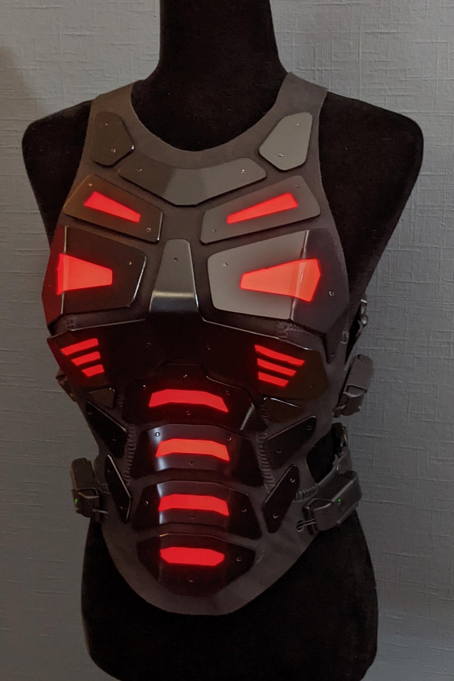 Mannequin wearing futuristic torso armor in black and grey with glowing red lights