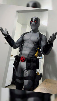 A person wearing a full Deadpool costume standing indoors in front of white doors. The costume includes metal shin guards and full protective metal gauntlets