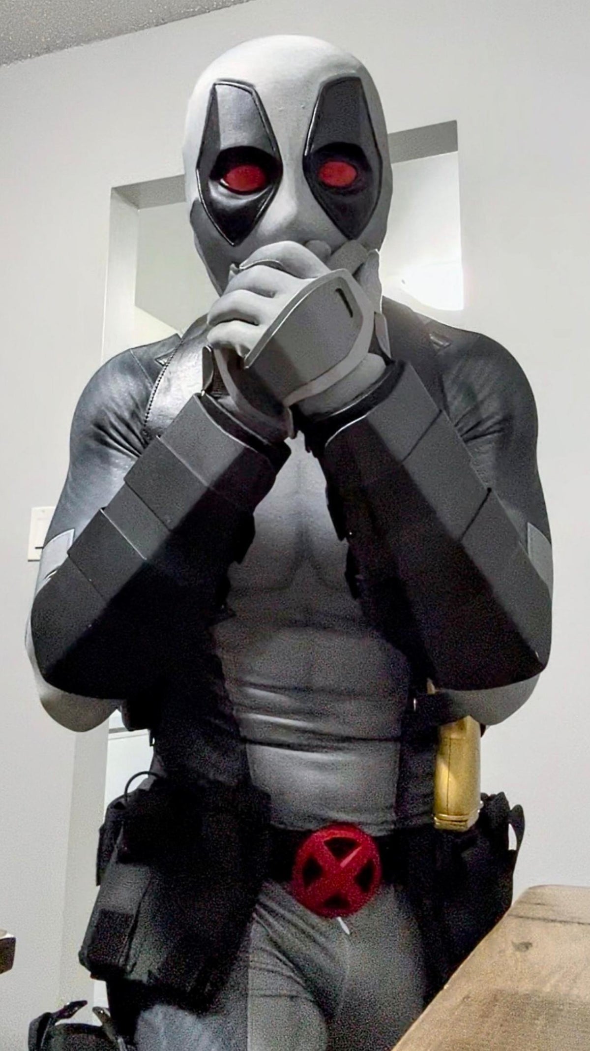 A person wearing a full Deadpool costume standing indoors. The costume includes full protective metal gauntlets