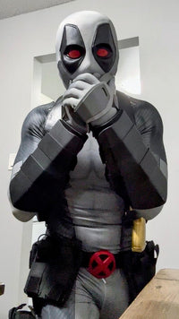 A person wearing a full Deadpool costume standing indoors. The costume includes full protective metal gauntlets