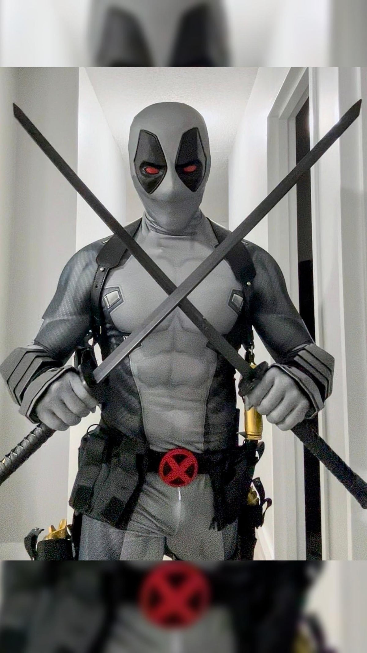 A person wearing a full Deadpool costume standing indoors The costume includes metal shin guards and full protective metal gauntlets