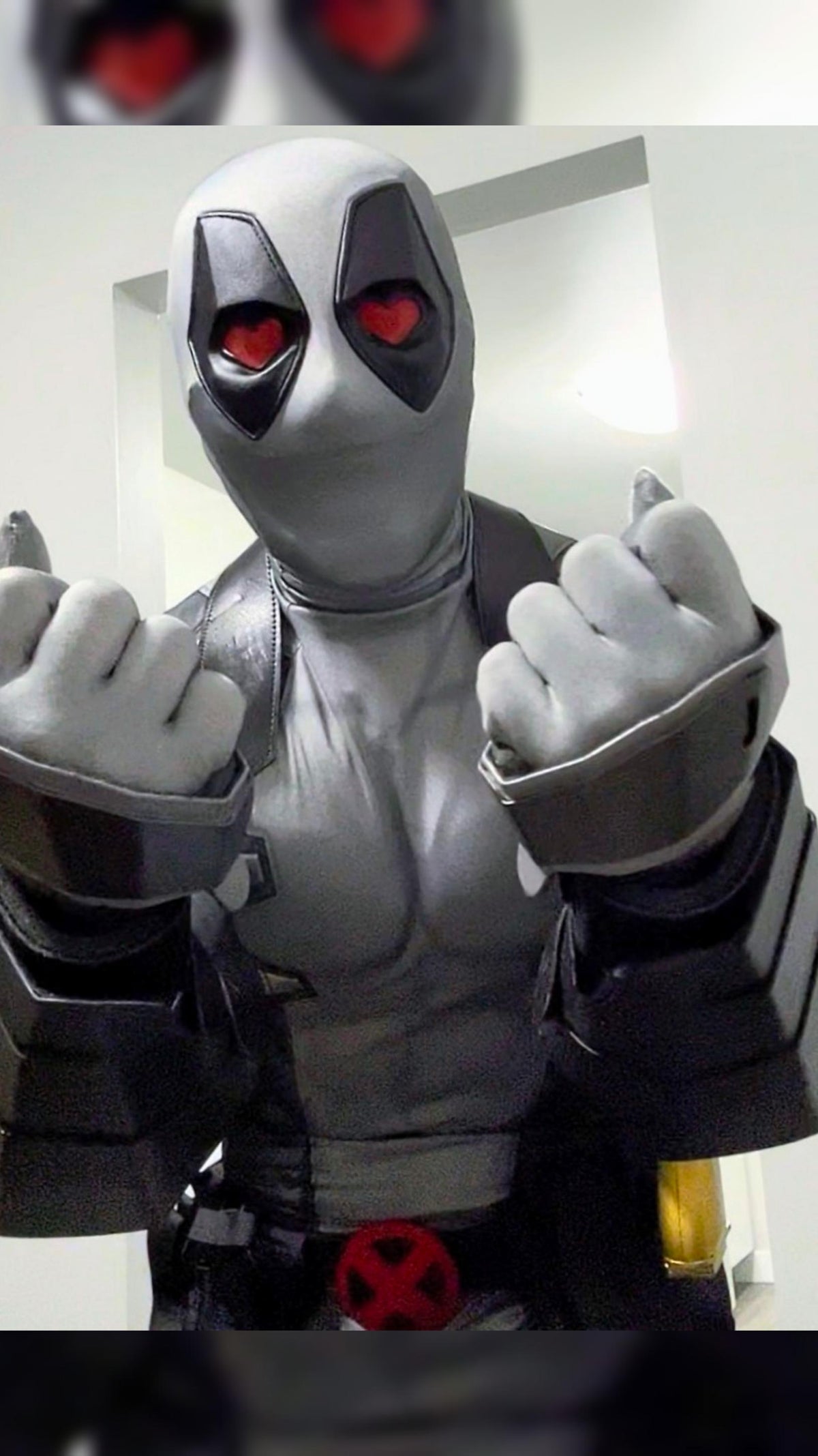 A person wearing a full Deadpool costume standing indoors with hearts in his eyes The costume featurses protective metal gauntlets held to the camera