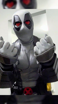 A person wearing a full Deadpool costume standing indoors with hearts in his eyes The costume featurses protective metal gauntlets held to the camera