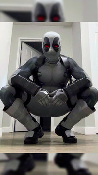 A person wearing a full Deadpool costume crouching indoors in front of white doors. The costume includes metal shin guards and full protective metal gauntlets
