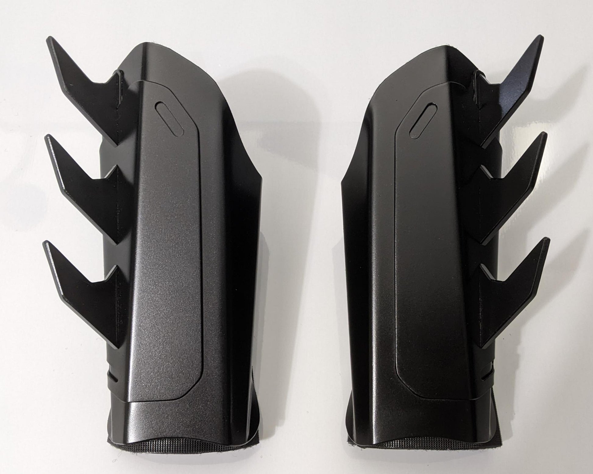 A pair of matte black metal batman arm guards or bracers with angular spikes, displayed side-by-side on a plain white background.