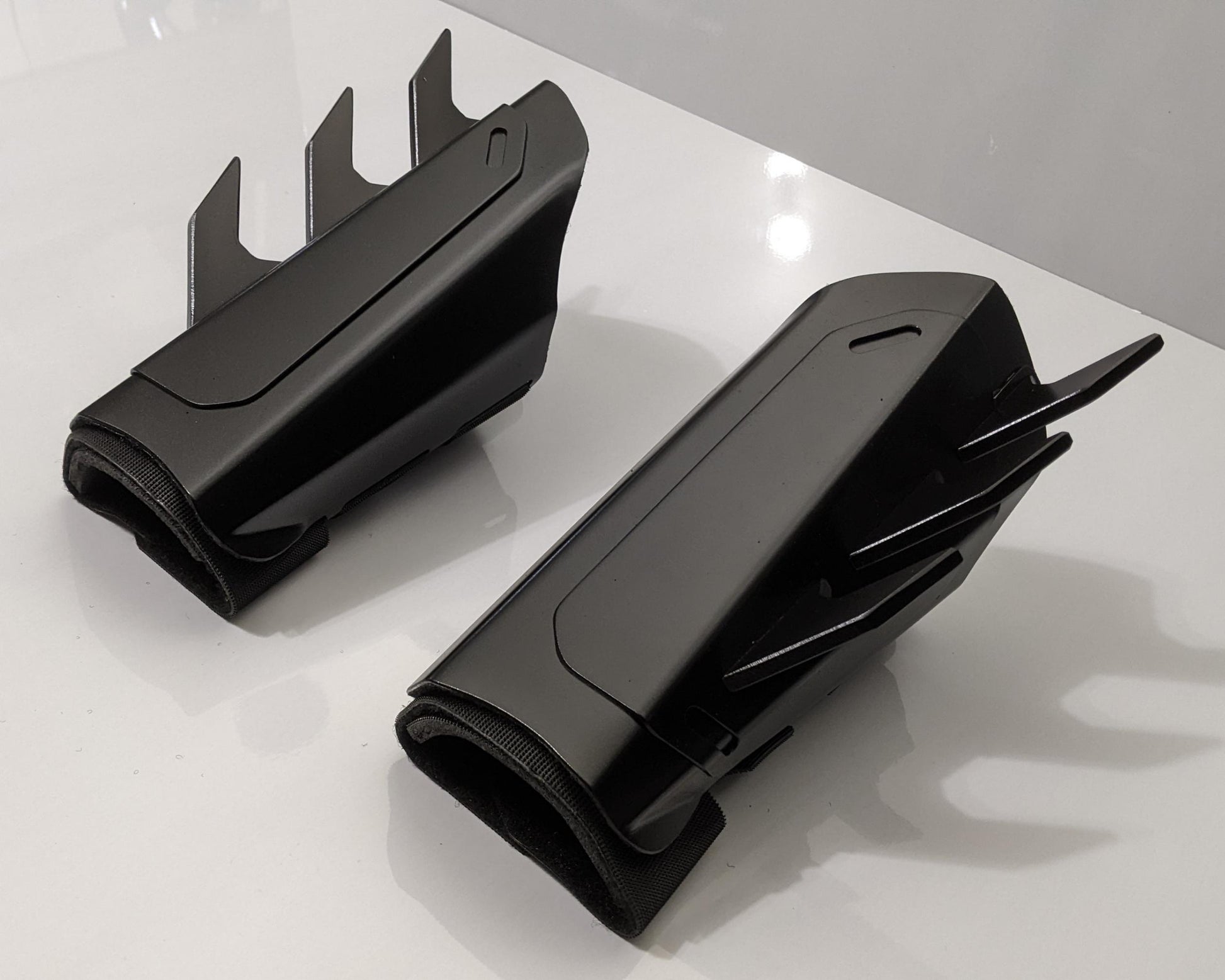 A pair of black protective metal batman guard covers with sharp upward and side spikes, displayed on a clean white surface.