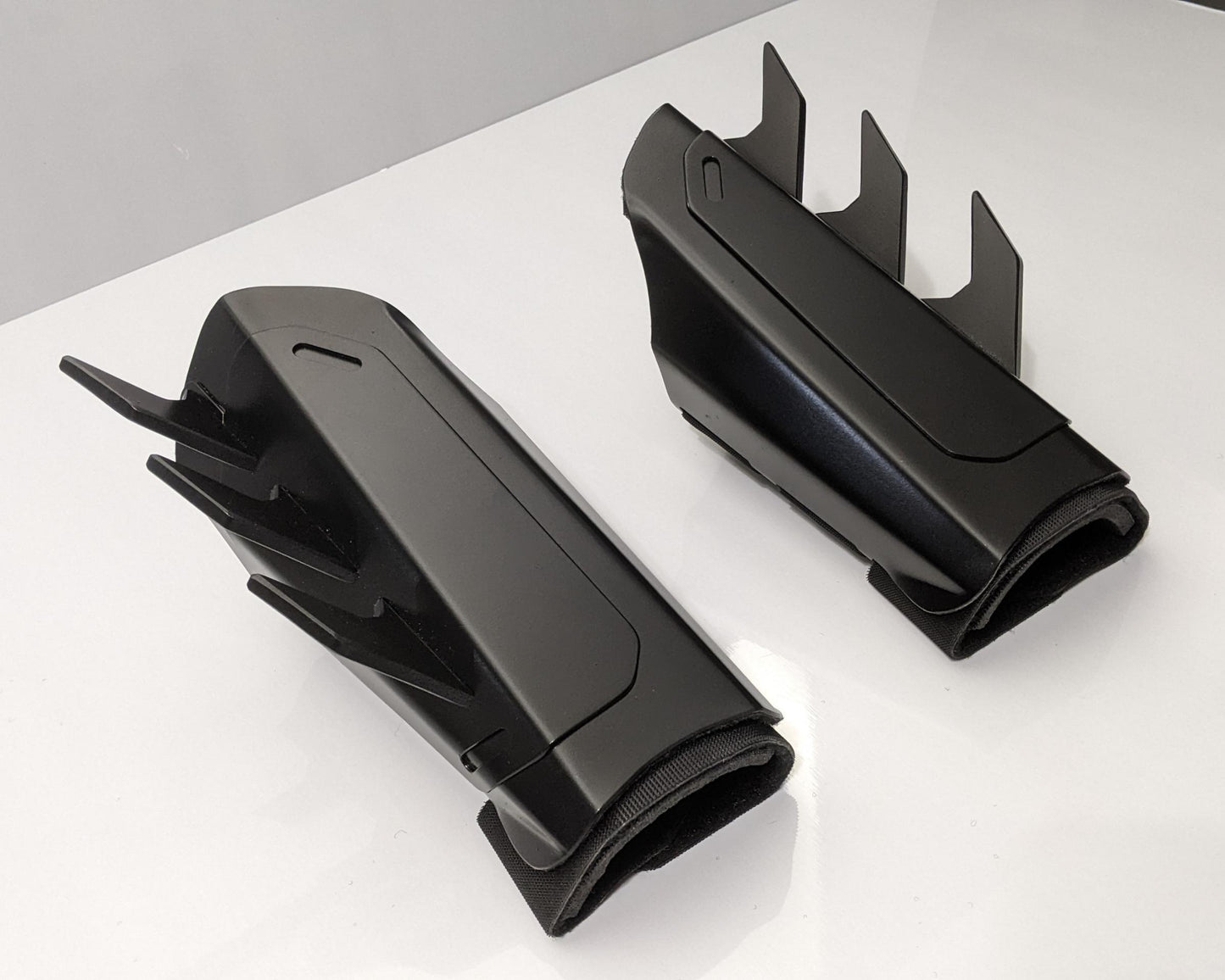 A pair of matte black protective armor metal batman bracers displayed on a clean white surface with a light gray background.