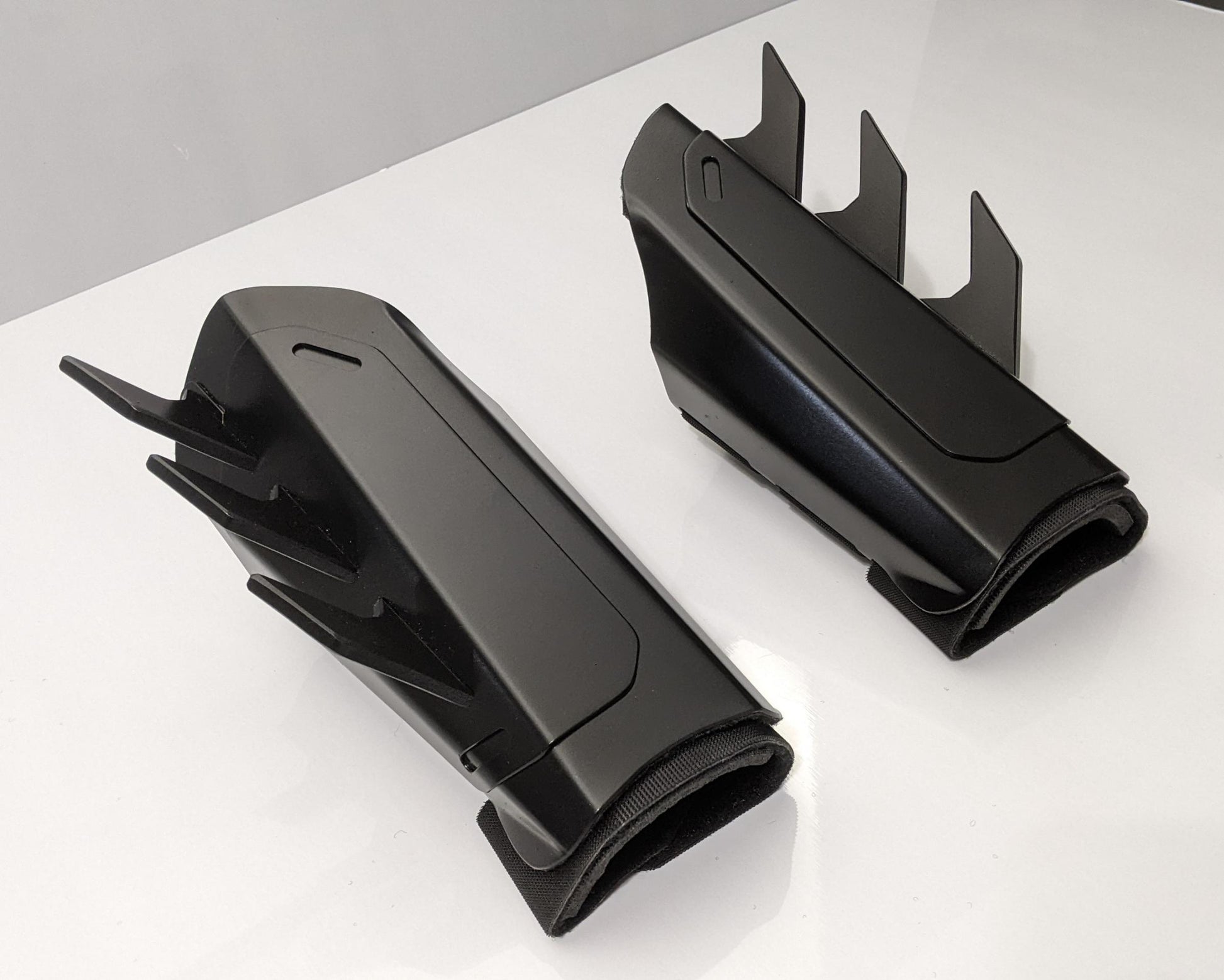 A pair of matte black protective armor metal batman bracers displayed on a clean white surface with a light gray background.