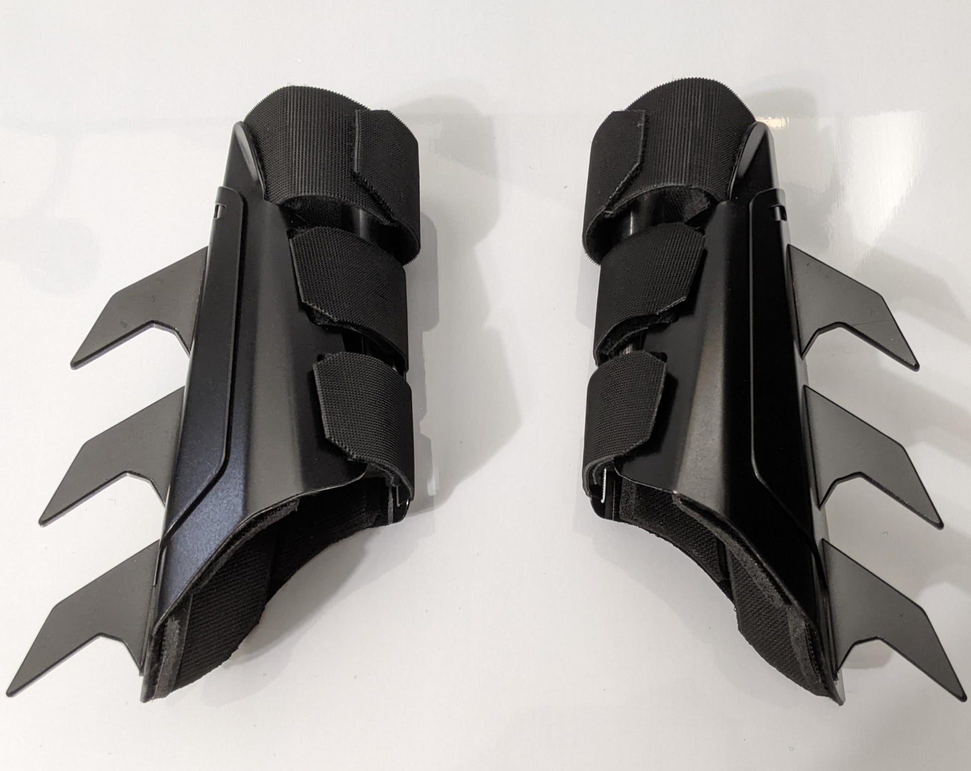 A pair of matte black protective armor metal batman bracers displayed on a clean white surface with a light gray background.