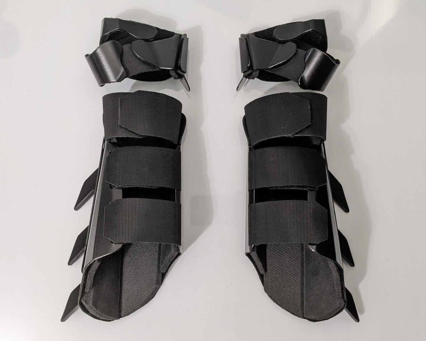 A pair of matte black protective armor metal batman bracers displayed on a clean white surface with a light gray background.