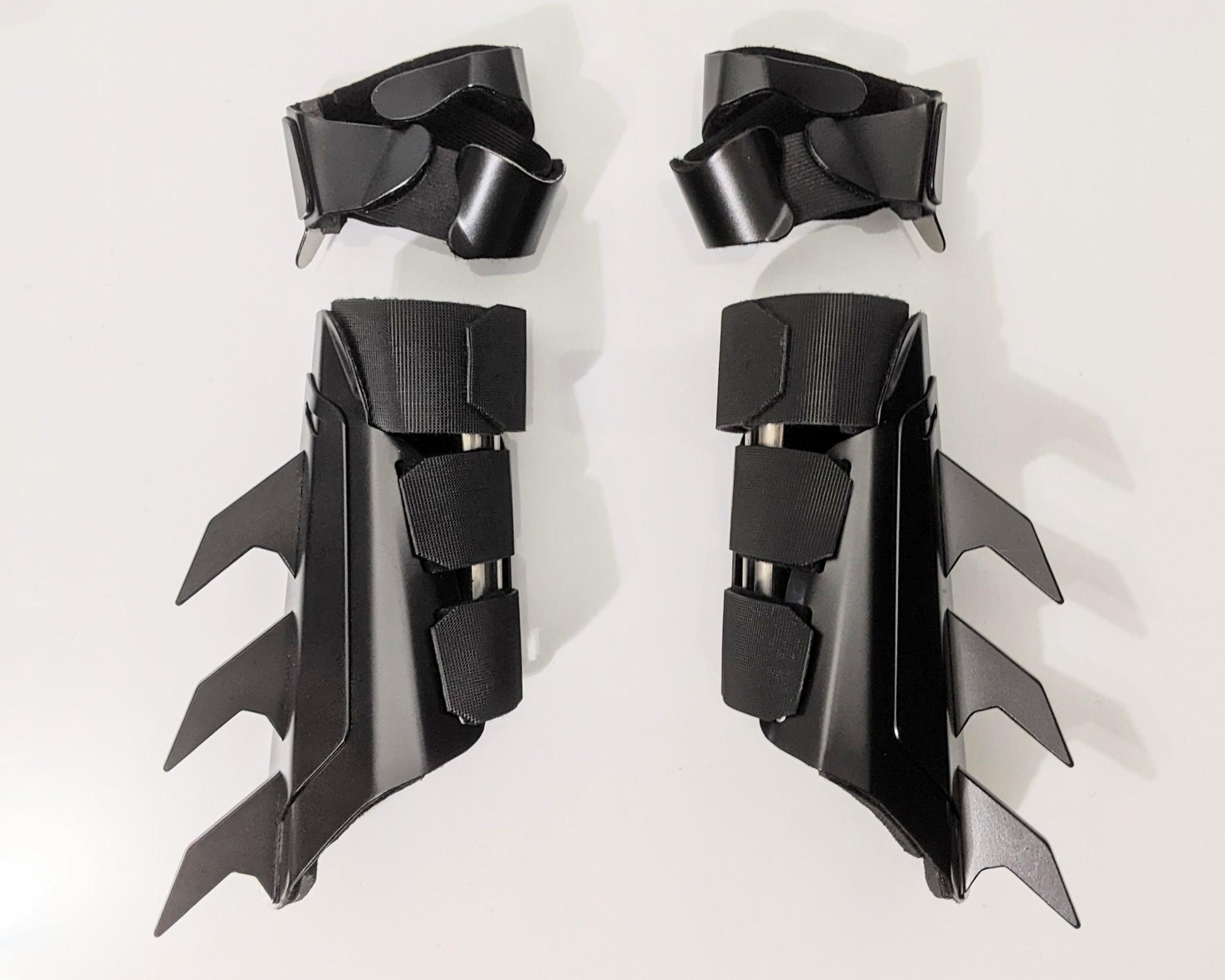 A pair of matte black protective armor metal batman bracers displayed on a clean white surface with a light gray background.