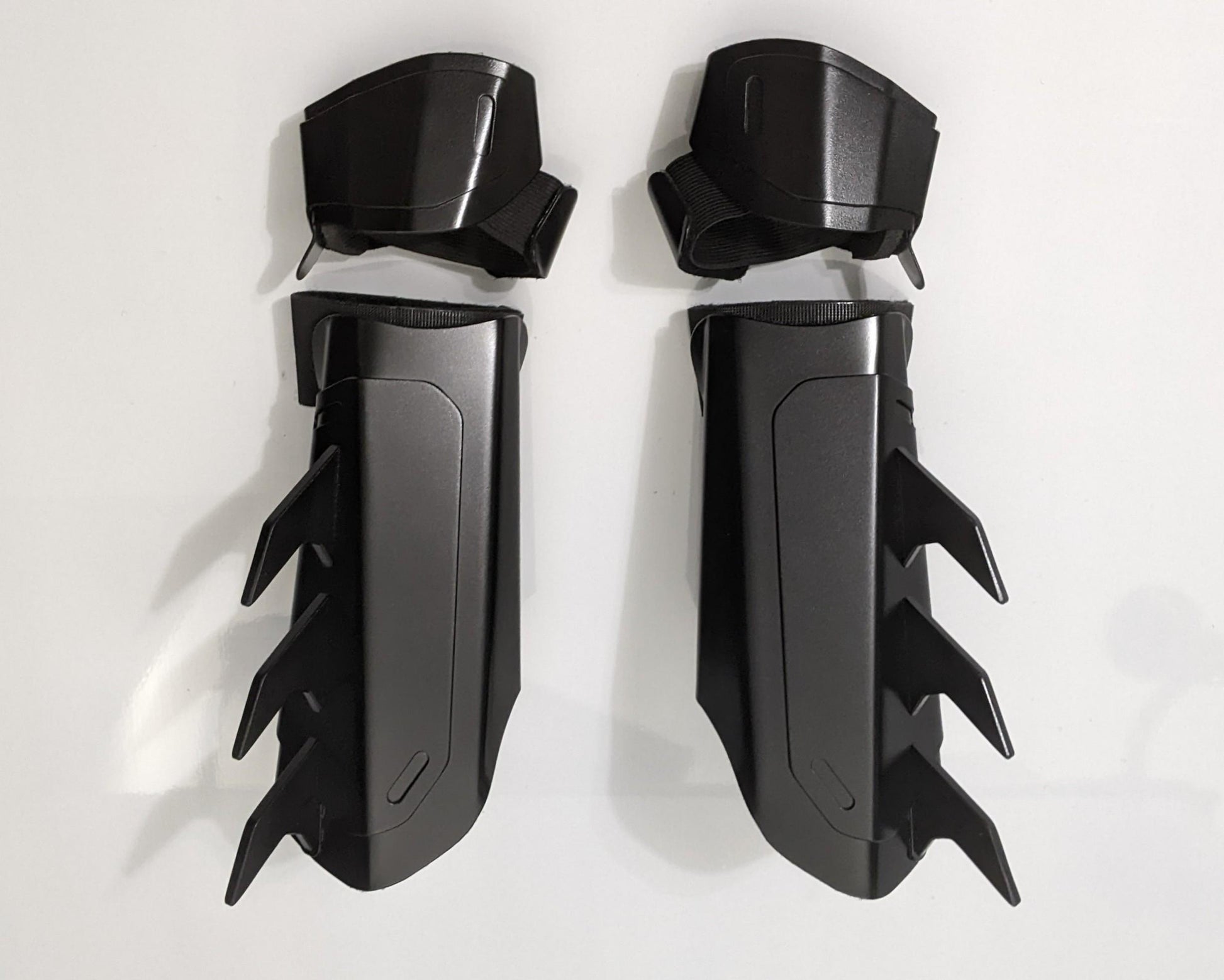 A pair of matte black protective armor metal batman bracers displayed on a clean white surface with a light gray background.