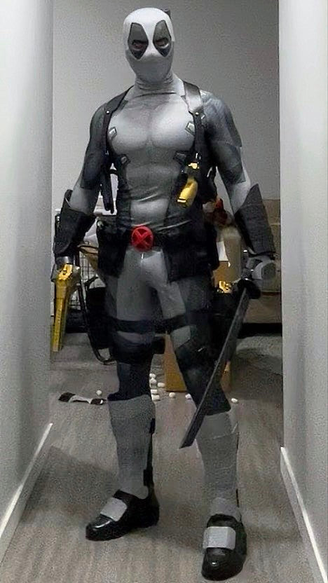 A person wearing a full Deadpool costume standing indoors. The costume includes metal shin guards and full protective metal gauntlets