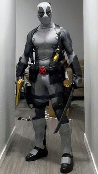 A person wearing a full Deadpool costume standing indoors. The costume includes metal shin guards and full protective metal gauntlets
