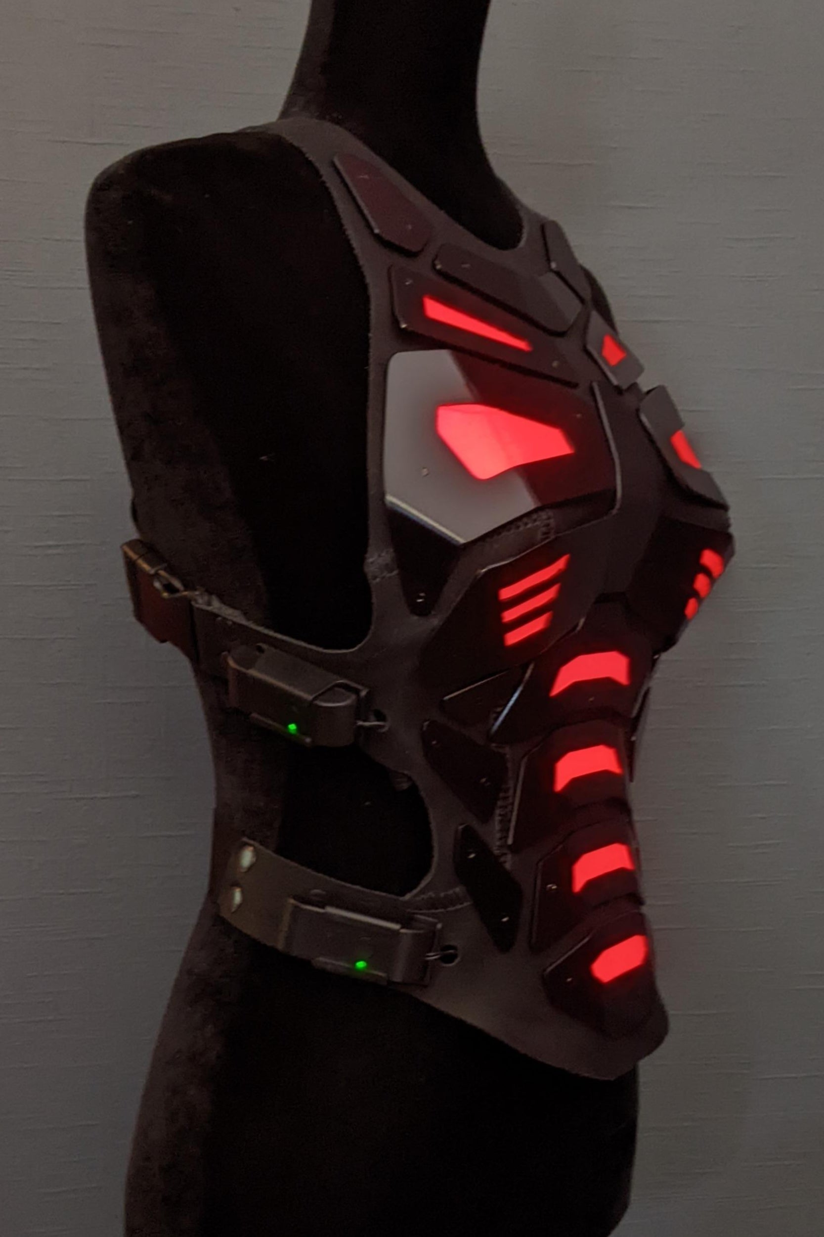 Mannequin wearing futuristic torso armor in black and grey with glowing red lights